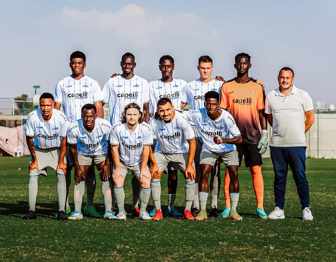 The TFA Dubai Pro Soccer Team poses for a group photo on the field, with players dressed in white jerseys and shorts. A coach stands on the right, exuding confidence. The sky is clear in the background, reflecting the team's bright future.